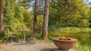 Eine Holzbank, ein Picknicktisch und eine Feuerstelle am See, mit einem Schild, auf dem 'KEHRE' steht.
