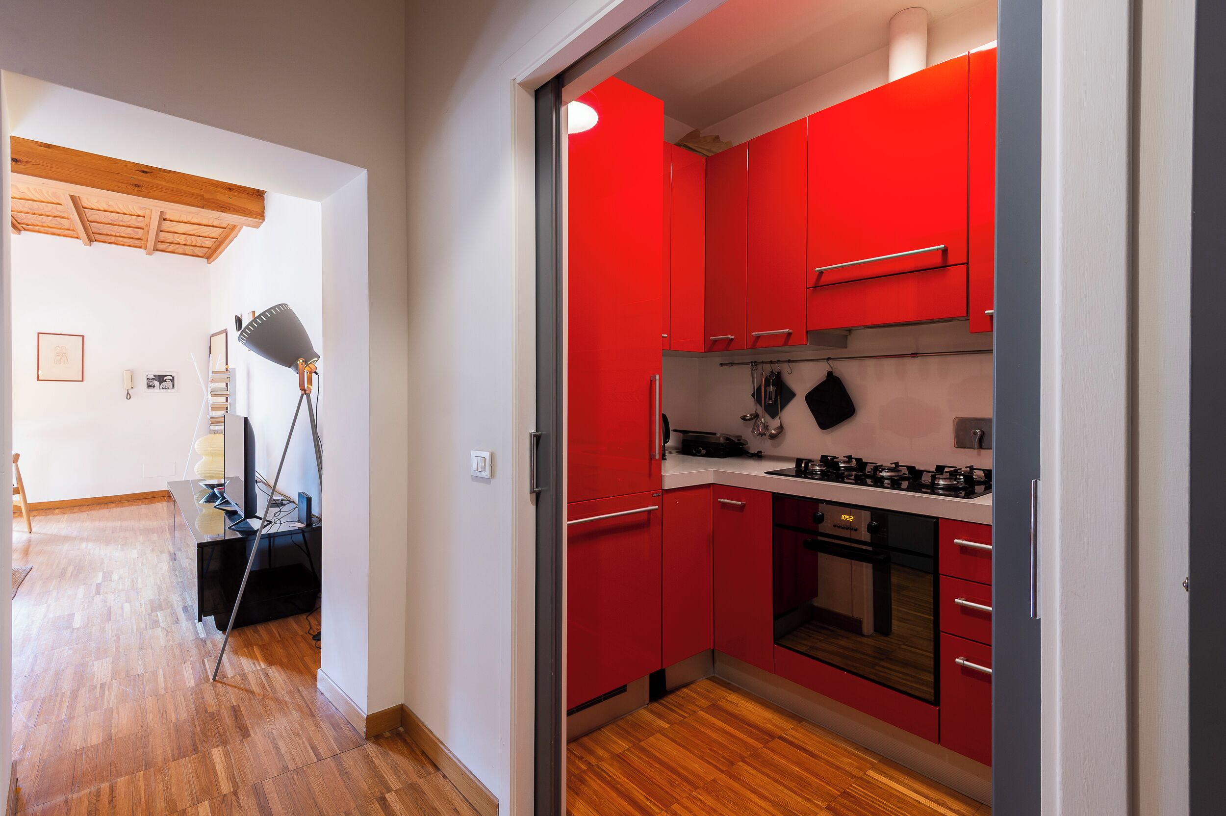 A modern kitchen with red cabinets, a gas stove, and a wooden floor.