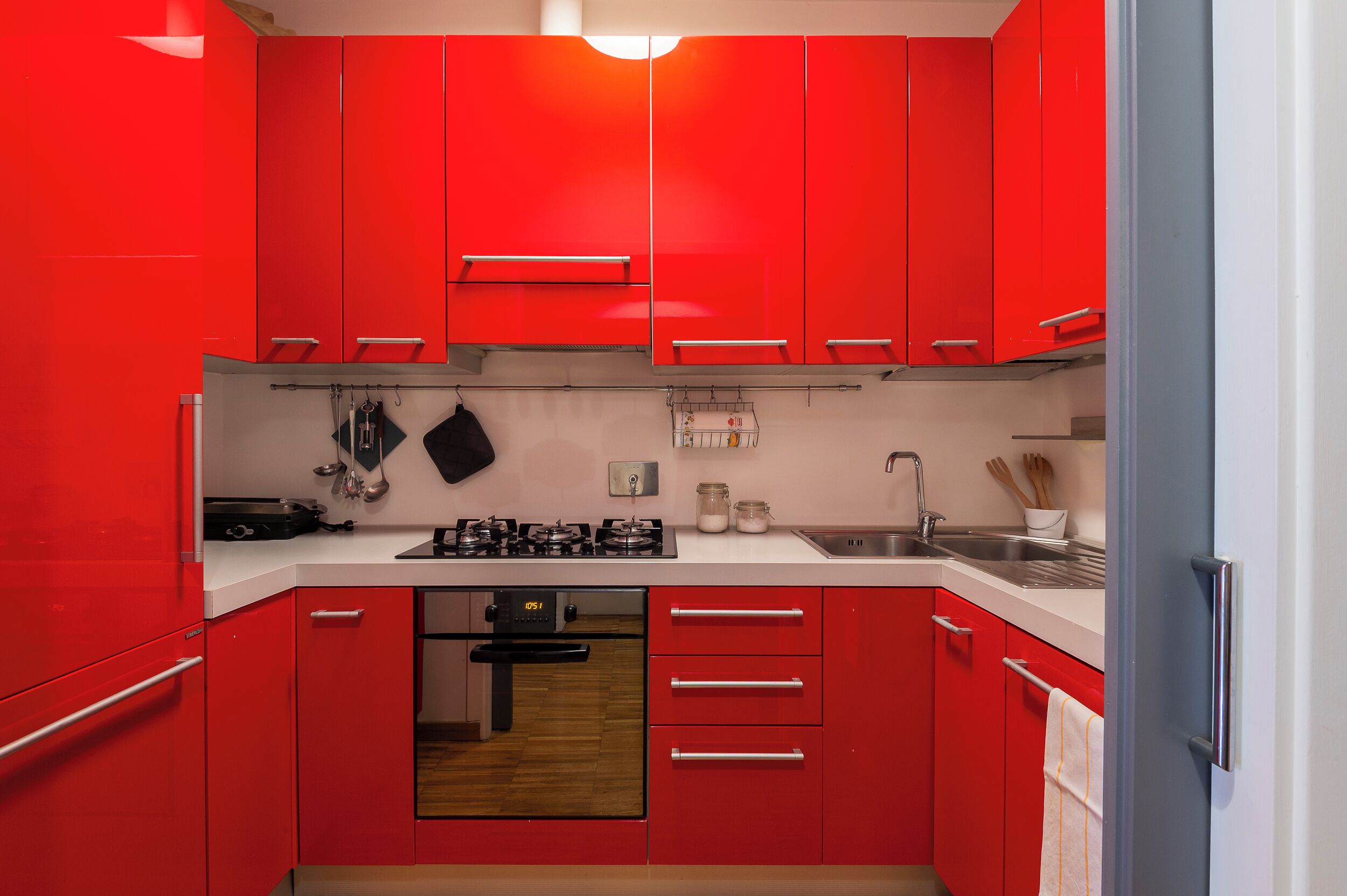 Una cocina moderna con armarios rojos, horno empotrado y electrodomésticos de acero inoxidable.