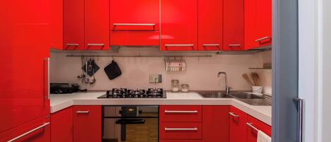 Una cocina moderna con armarios rojos, horno empotrado y electrodomésticos de acero inoxidable.