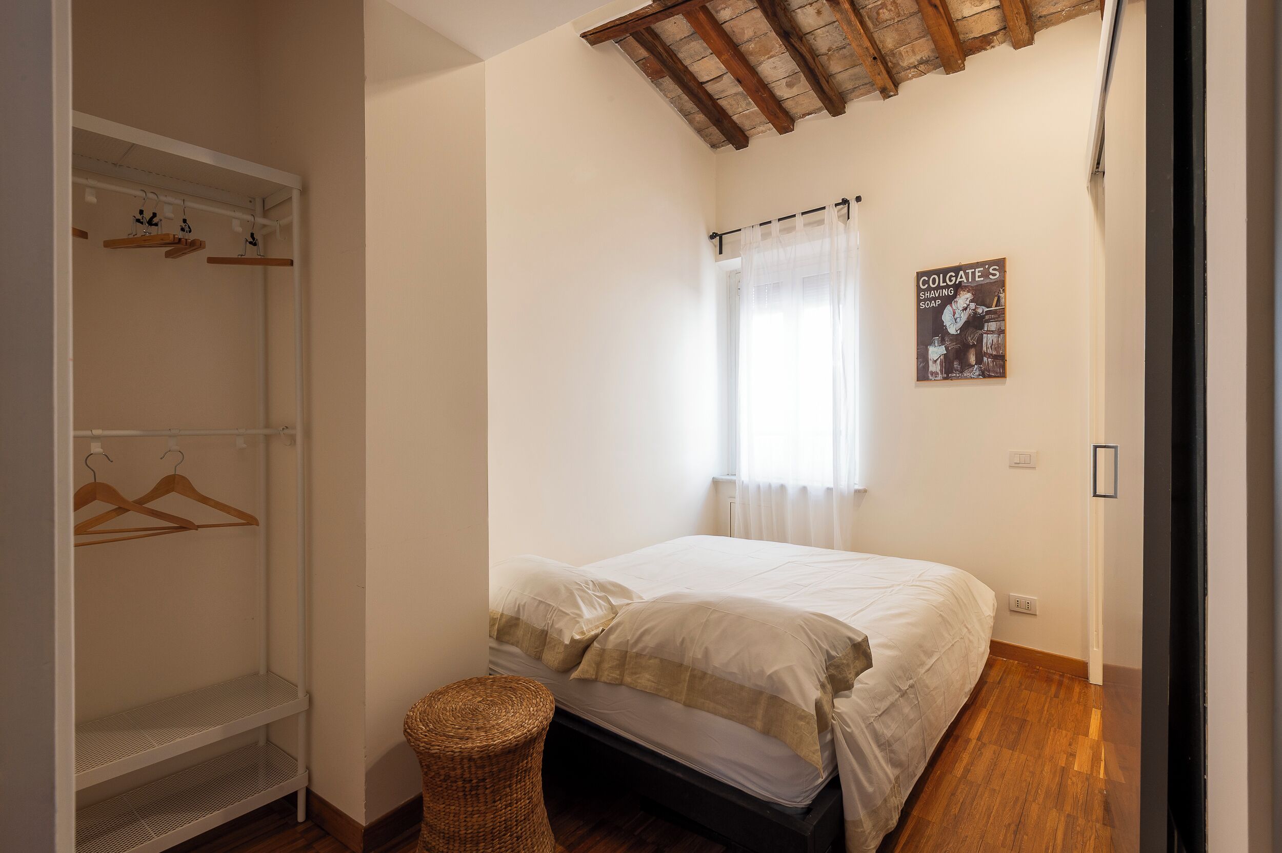Une chambre à coucher avec un lit, une armoire, un porte-chaussures suspendu, un panier en osier et une affiche accrochée au mur.