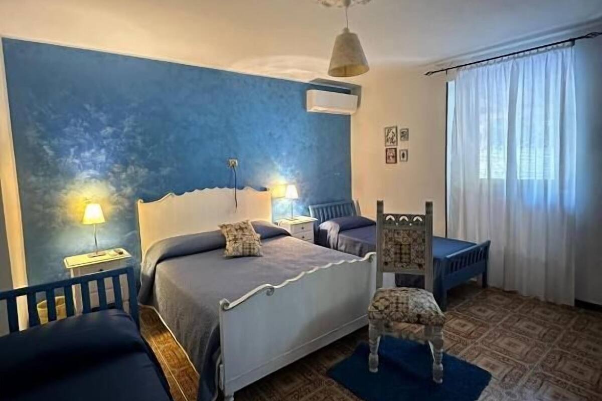 A bedroom with a bed, bedside tables, a chair, a patterned rug, and a window with curtains.