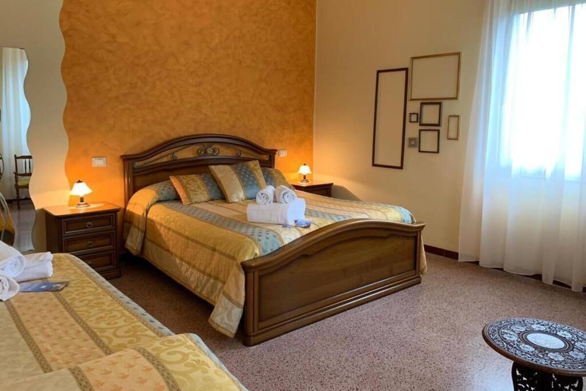 A hotel room with a large bed, two bedside tables, a round table, and a window with curtains.