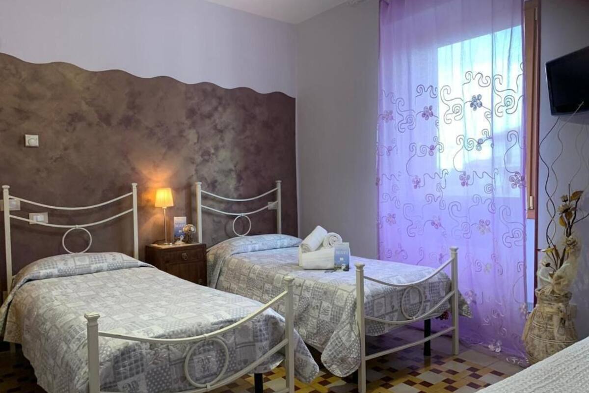 A room with two beds, a nightstand, a lamp, a television, and a window with curtains.