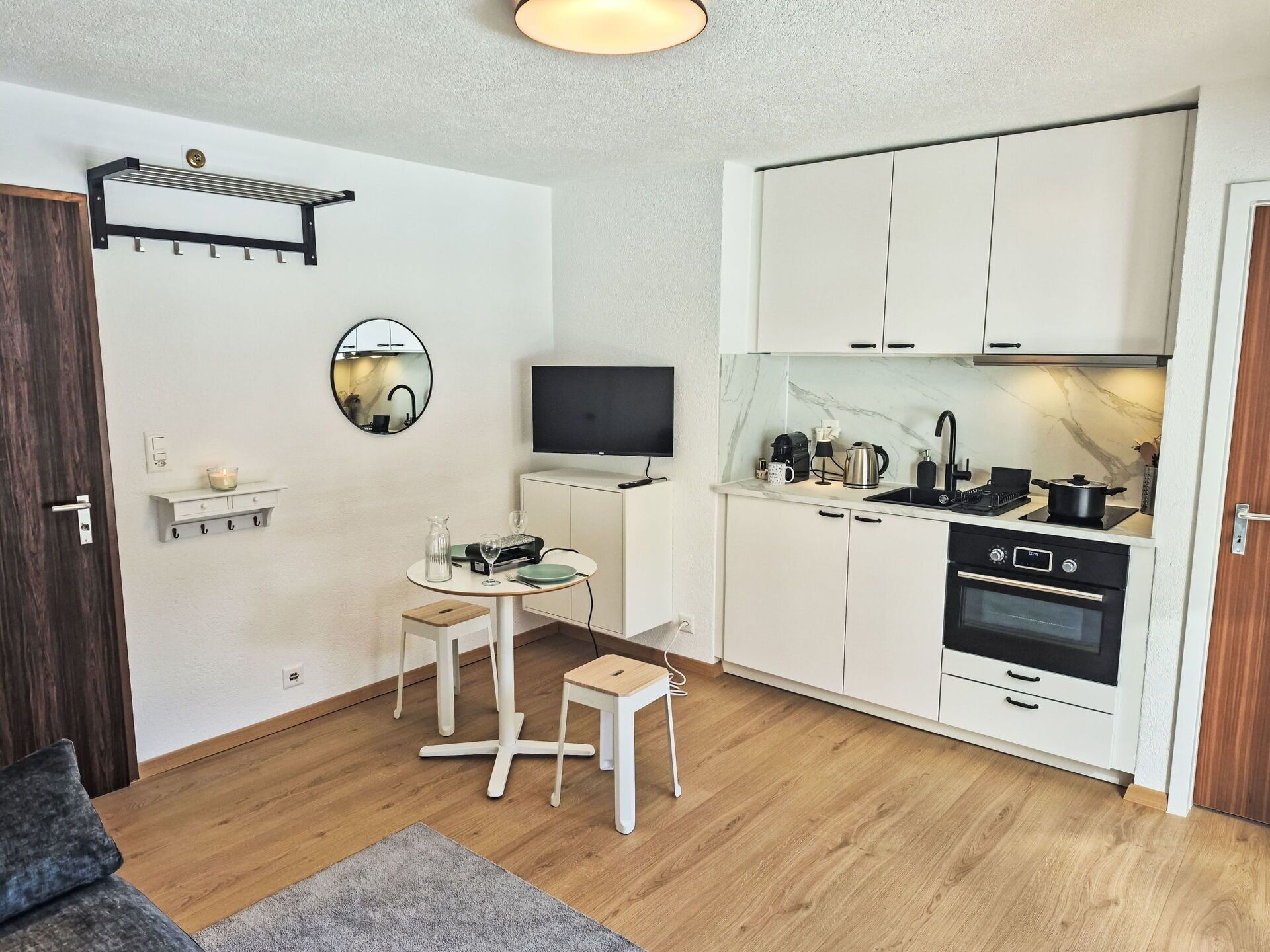A compact kitchen with white cabinets, a black stove, and a small dining area with stools.