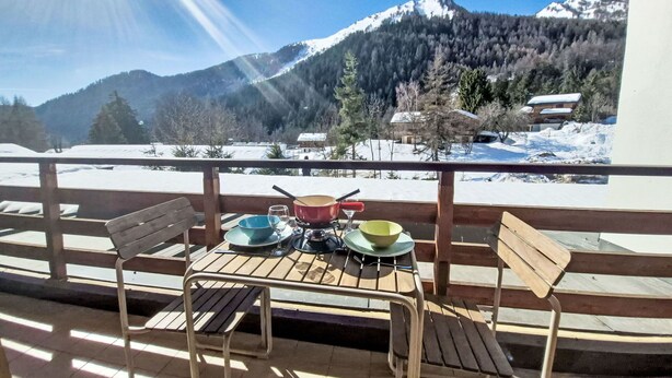 Un balcón con una mesa lista para dos personas, con vistas a un paisaje montañoso nevado.
