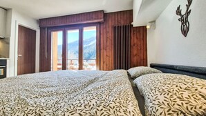 Un dormitorio con dos camas, techo de madera, vista a las montañas y un balcón con mobiliario exterior.