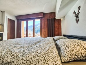A bedroom with two beds, a wooden ceiling, a view of mountains, and a balcony with outdoor furniture. - Lovely apartment for 2 people with WIFI, TV, balcony and pets allowed (Ovronnaz)