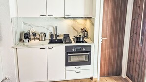 Una cocina pequeña con gabinetes blancos, un lavamanos negro, una estufa y un horno.