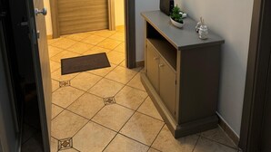 Un couloir avec une porte en bois, une petite console sur laquelle est posée une plante, et un luminaire fixé au mur.