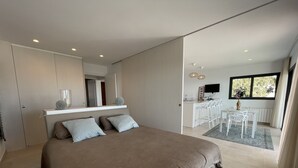 Ein modernes Schlafzimmer mit einem großen Bett, einem Einbauschrank, einer kleinen Küchenzeile und einem Essbereich mit weißer Möbel.