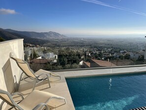 A poolside area with lounge chairs, a clear view of a town and mountains in the distance, and a tiled pool. - Ref. Ali12 Modern villa with private pool and sea view (Rosas / Roses)