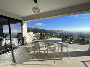 Un balcone con tavolo e sedie, una bottiglia di vino e vista su una città e montagne.
