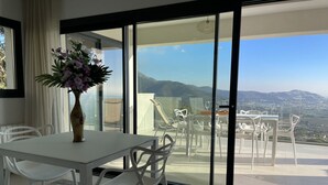 Ein modernes Zimmer mit einem weißen Tisch und Stühlen, einer Vase mit Blumen und einem Balkon mit Blick auf die Landschaft.