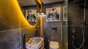 A modern bathroom with a stone sink, toilet, and shower. There are framed pictures on the wall. - WM Cappadocia (Nevşehir)