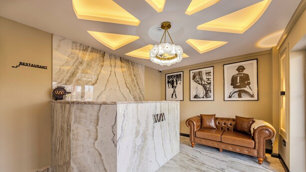 A marble reception desk with a logo, a brown leather sofa, and framed artwork on the wall. - WM Cappadocia (Nevşehir)