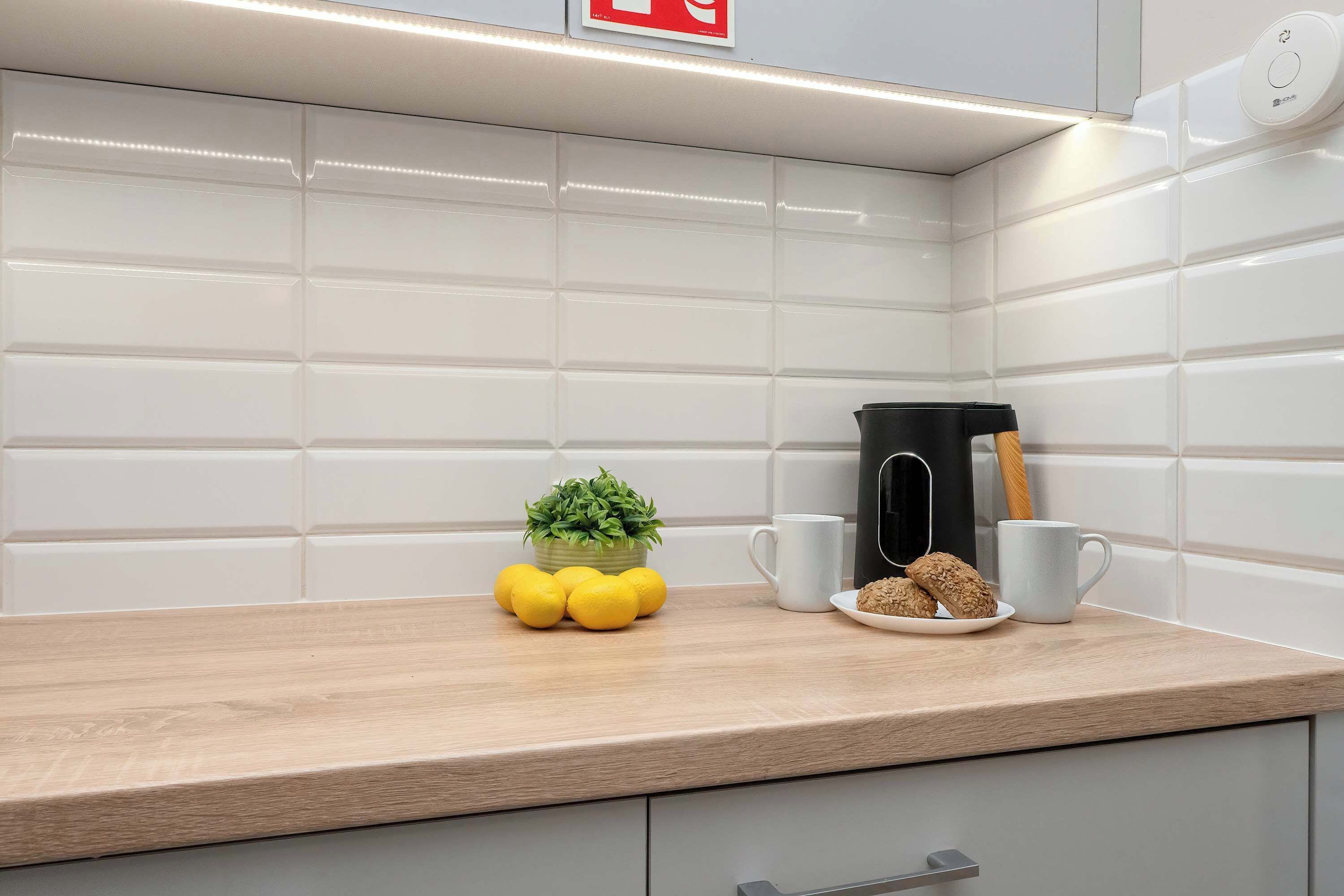 Una cocina con encimera de madera, cafetera, planta pequeña, limones y un plato con galletas.