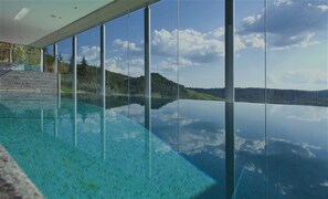 Vista clara d'una piscina amb una barrera de vidre que reflecteix el paisatge i el cel circumdants.
