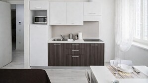 A modern kitchen with white cabinets, a microwave, and a sink. There is a dining area with a table set for two. - Hotiday Trieste Corso Italia (Trieste)
