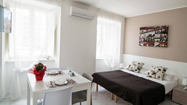 A bedroom with a bed, bedside table, and a window with curtains. - Hotiday Trieste Corso Italia (Trieste)
