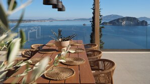 Ein Holztisch mit gewebten Untersetzern und Korbstühlen, mit Blick auf eine malerische Küstenlandschaft mit Bergen und einem Gewässer.
