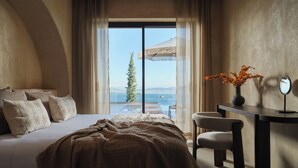Ein Schlafzimmer mit einem großen Bett, einem Schreibtisch, einem Sessel und Meerblick durch ein Fenster.