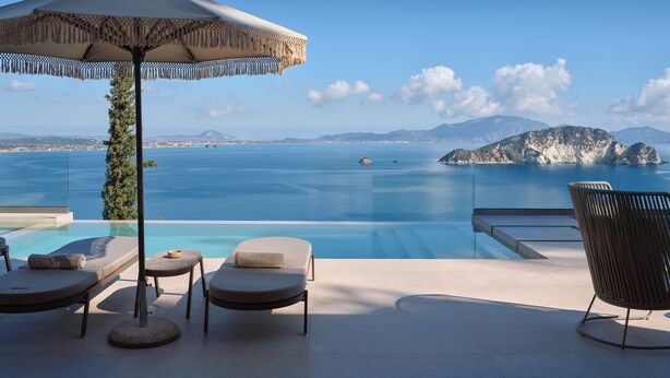 Ein moderner Außenbereich mit Lounge-Möbeln, einem Pool, Liegestühlen und einem Sonnenschirm mit Blick auf ein malerisches Gewässer und entfernte Inseln.