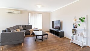 A modern living room with a grey sofa, a black coffee table, a flat-screen TV, and a white bookshelf.