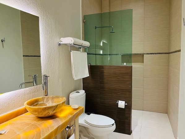 A bathroom with a wooden vanity, a glass shower enclosure, a toilet, and a mirror.
