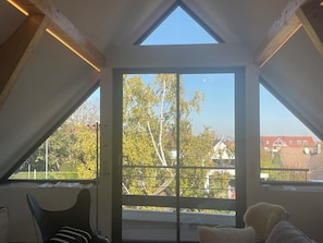 A room with a sloped ceiling, large windows, and a view of trees and buildings outside. - The vineyard setting, the luxurious gite (Wettolsheim)