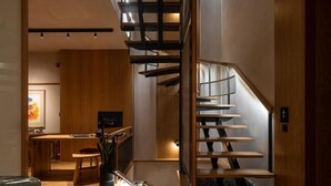 A modern interior with a wooden staircase, a kitchen area, and a dining space. - Santa Clara Hotel (Chania)