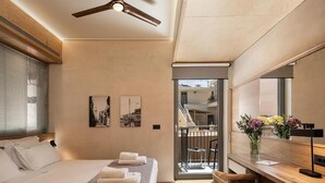 A hotel room with a bed, a desk, a chair, a ceiling fan, a window with blinds, and a balcony door. - Santa Clara Hotel (Chania)