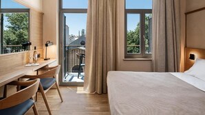 A hotel room with a bed, desk, chair, and large windows. - Santa Clara Hotel (Chania)