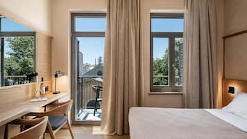 Habitación de hotel con cama, escritorio, silla y ventanas amplias.