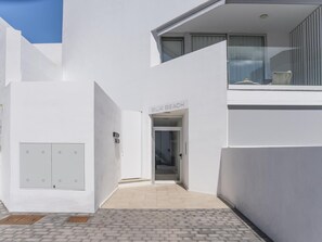 Ein modernes Gebäude mit weißer Fassade, einem sichtbaren Eingang mit der Aufschrift "BIK BEACH" und einem kleinen Balkon mit einem Stuhl.