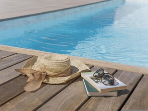 A wooden deck by a pool with a straw hat, sunglasses, and a book. - CHL Naos del Mar, lovely place pool beach (Los Llanos de Aridane)