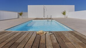 A rectangular pool with a wooden deck, two potted plants, and a pair of sunglasses and a book on the deck. - CHL Naos del Mar, lovely place pool beach (Los Llanos de Aridane)