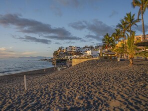 A beach with a rocky shoreline, palm trees, and buildings in the background. - CHL Naos del Mar, lovely place pool beach (Los Llanos de Aridane)