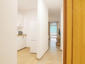 Ein schmaler Flur mit Küchenzeile links, Holzboden und Blick auf einen Balkon mit Streifen-Vorhängen.
