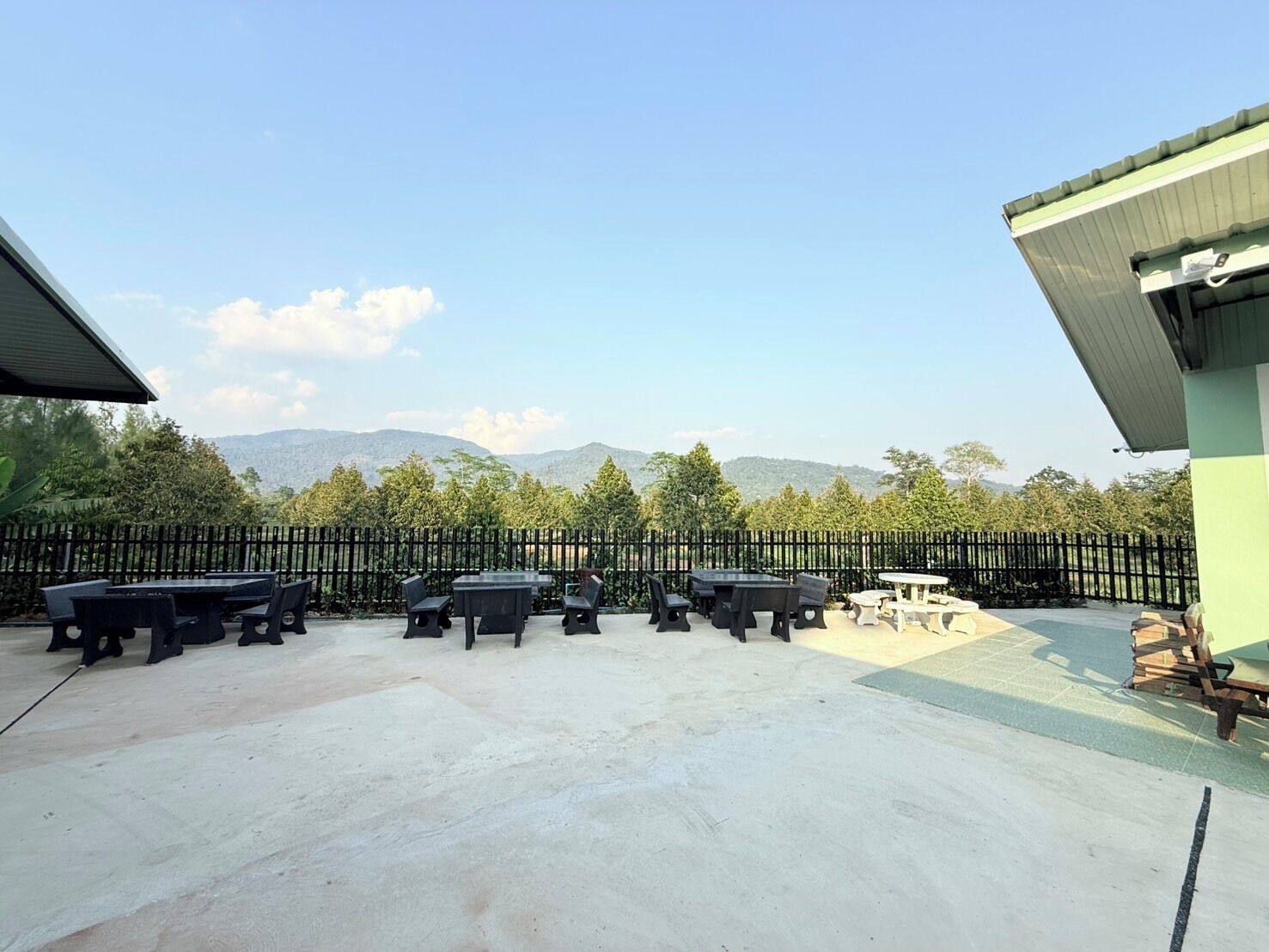 An outdoor patio with tables and chairs, a fenced area, and a view of mountains.