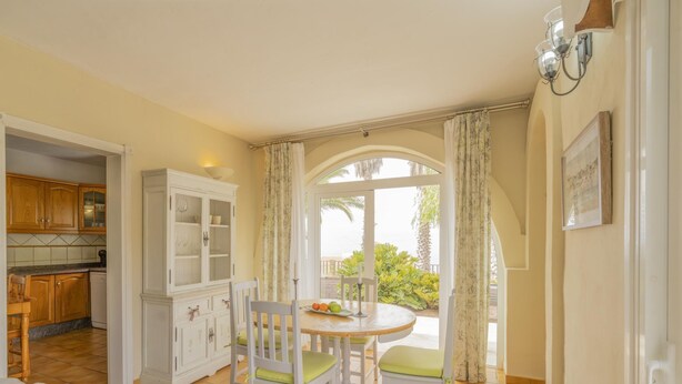 A dining area with a round table and chairs, a kitchen with wooden cabinets, and a view of greenery outside. - CHL La Concepción, Adeje: amazing sea views (Adeje)