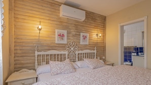 A bedroom with a wooden wall, a white bed with floral bedding, two wall-mounted lights, and a small bedside table. - CHL La Concepción, Adeje: amazing sea views (Adeje)