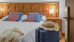 A hotel room with a wooden headboard, a bed with patterned pillows, a bedside lamp, a suitcase, and a hat on the floor. - CHL El Faro, next to the Puerto Naos beach (Puerto Naos, Los Llanos de Aridane)