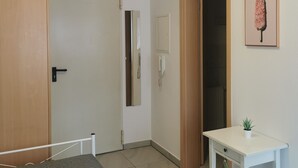 Un dormitori amb un llit, una taula de nit amb una planta, una porta, un mirall i un lluminària fixat a la paret.