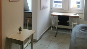A room with a desk, a chair, a bed, and a window.