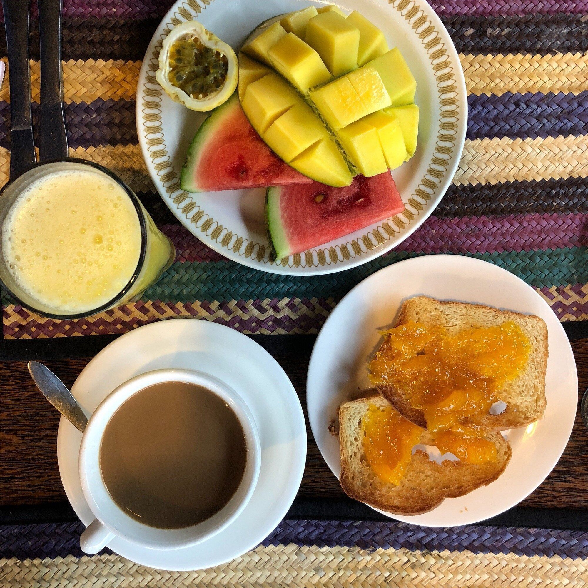 A breakfast setting with a plate of fruit, toast with jam, a cup of coffee, and a glass of juice.