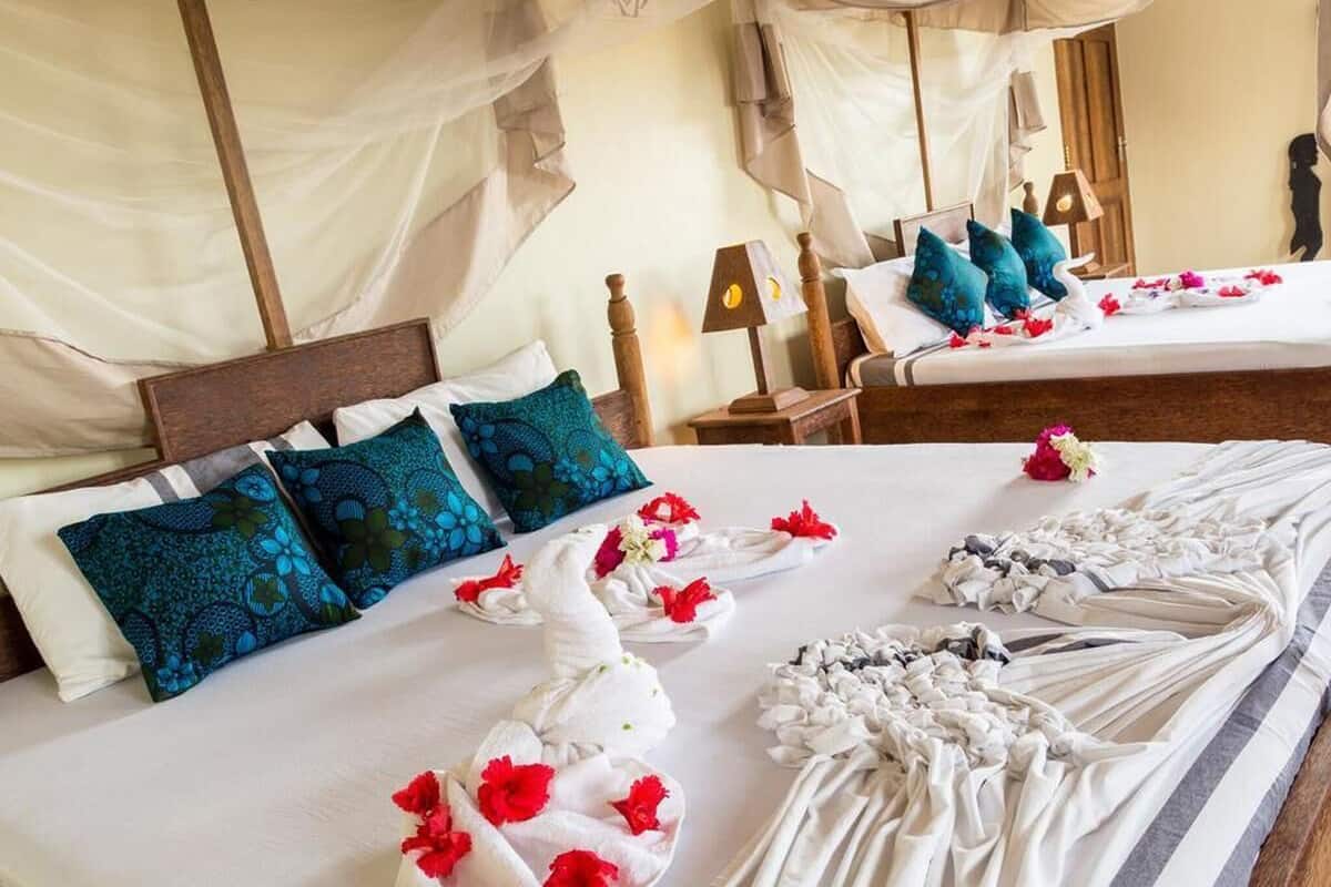 Una habitación de hotel con una cama, almohadas, una mesita de noche, una lámpara y un espejo.