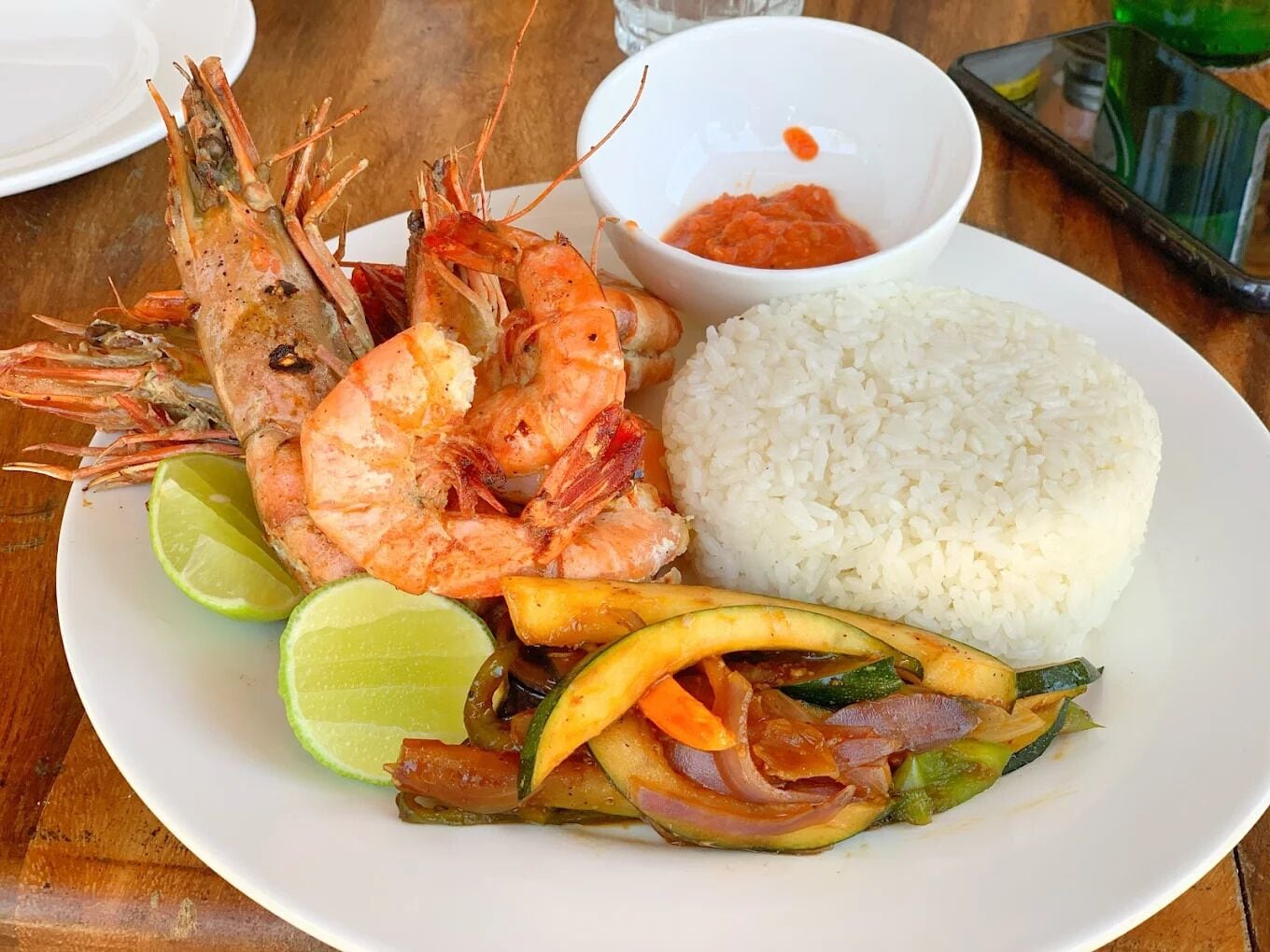 A plate with cooked shrimp, white rice, and a vegetable stir-fry, accompanied by a lime wedge and a small bowl of sauce.