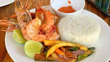 A plate with cooked shrimp, white rice, and a vegetable stir-fry, accompanied by a lime wedge and a small bowl of sauce.