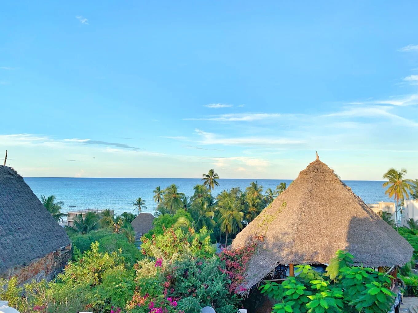 Thatched-roof huts surrounded by lush greenery and a view of the ocean.